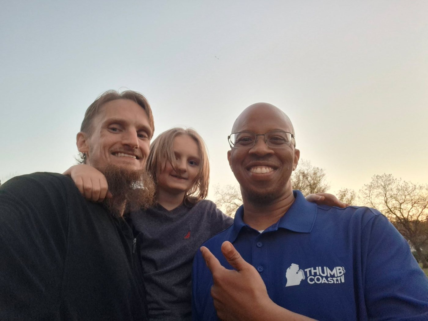 Andrew Artman with his son and Choze Powell of Thumb Coast TV, smiling at sunset in Port Huron